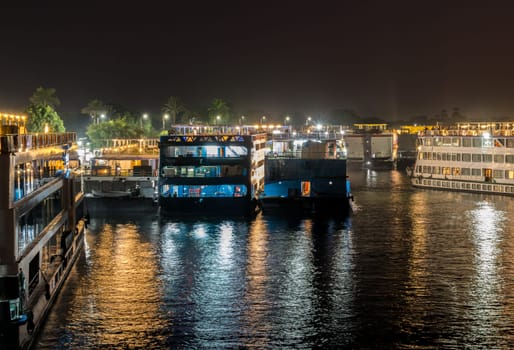 Illuminated Egyptian Nile cruiseboats stacked along the riverbank at Kom Ombo for temple visit
