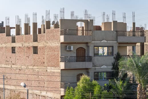 An unfinished building in Esna, Egypt, with brick and concrete construction and rebar on roof. Some apartments occupied