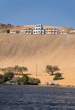Fast flowing water of the River Nile near Aswan Egypt with Nubian vacation resort on hilltop