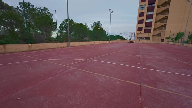 A serene view of a vibrant red basketball court amid lush greenery and nearby residential buildings