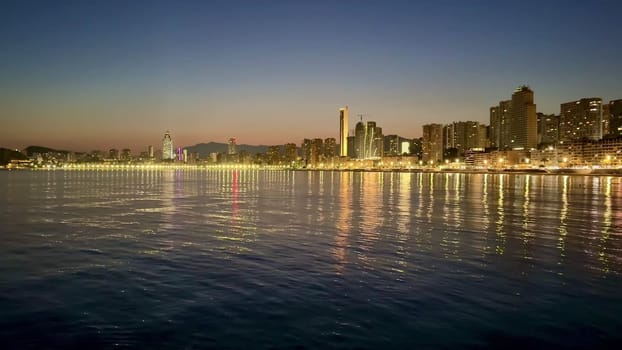 A captivating sunset view of a modern city skyline along the water's edge, reflecting lights across the surface.