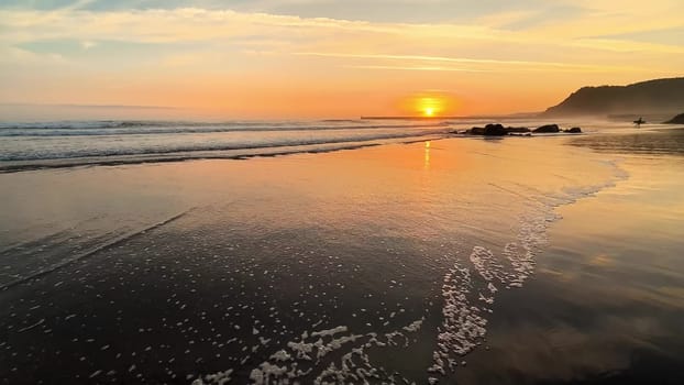 This is a captivating view of a beautiful sunset reflecting on the calm ocean waves by the serene beach