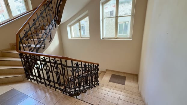 A grand staircase with an ornate railing and natural light from large windows creates a captivating atmosphere