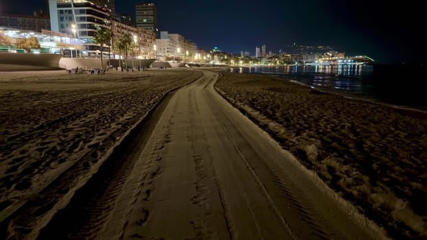 A serene beach pathway illuminated by nighttime city lights, perfect for relaxation and tranquility.