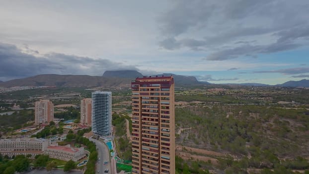 Aerial shot showing tall urban buildings with majestic mountains and lush green landscapes in the backdrop