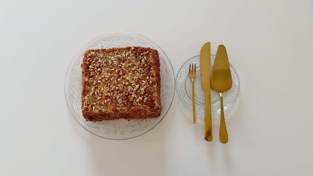 A beautifully plated square cake, generously topped with a mix of nuts, elegantly paired with luxurious golden cutlery