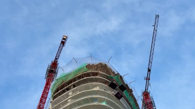 Capturing the ongoing construction of a highrise building, featuring cranes and scaffolding all around it