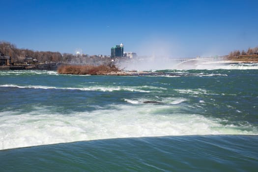 Visitors admire the breathtaking views of Niagara Falls under clear skies, as the majestic waterfall cascades powerfully into the river.