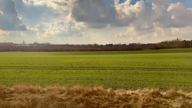 A serene view showing a lush and vibrant green field bordered by gentle rolling hills and scattered white clouds