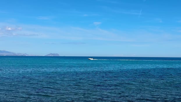 A sleek, fast speedboat glides effortlessly through the crystalline blue waters under a bright, clear sky