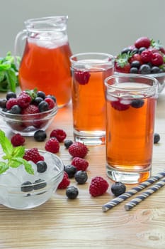 Colorful berry drinks filled with ice cubes and adorned with fresh berries create a vibrant display on a wooden surface, accompanied by mint leaves for added freshness.