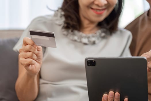 Senior couple happily shopping online using a tablet and credit card, embracing modern technology in the comfort of their home.