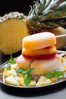 Mango pineapple ice cream stacked on a silver platter is garnished with mint leaves and accompanied by freshly cut fruit. Tropical pineapples add to the vibrant atmosphere.