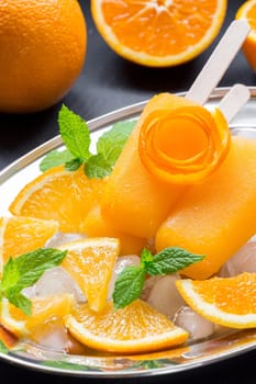 Vibrant orange icecream sits on a silver platter accompanied by fresh orange slices and mint leaves, creating a refreshing dessert perfect for hot summer days.