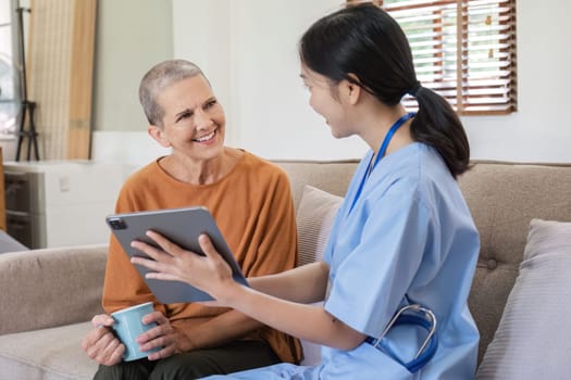 A young nurse offers health care advice to an elderly woman, using a digital tablet in a cozy home environment.