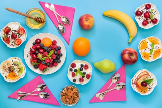 6 bowls of yogurt dressed with different ingredients fruit, berries, nuts, honey, and 6 spoons, napkins and right up some empty space on light blue background. Horizontal. Top view.