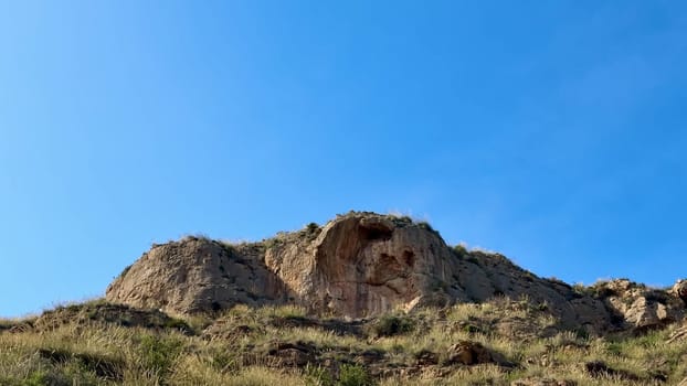 A breathtaking and stunning view of a unique rock formation surrounded by lush, vibrant grasslands beneath a clear sky