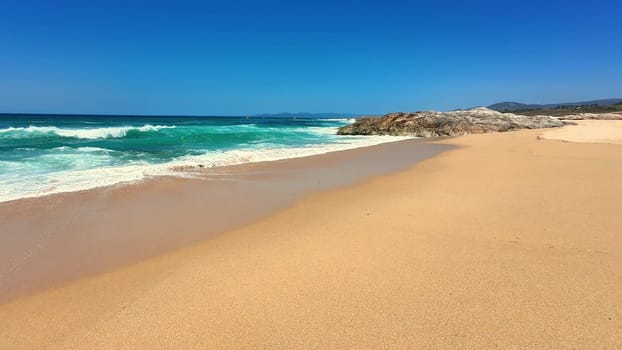 A tranquil beach scene showcasing turquoise waves lapping at soft golden sand under a bright blue sky.