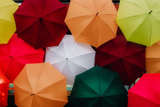 Beautiful view of many colorful and multicolored open umbrellas installed on the wall indoors in a public park on a sunny spring day, side view very close-up. Concept colorful backgrounds and textures.
