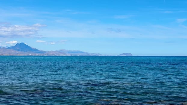 A stunning and beautiful coastal view showcasing the vast ocean, distant majestic mountains, and a clear blue sky