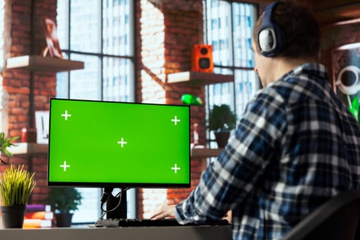 Freelancer listening music, analyzing data on isolated screen PC monitor at desk, compiling analytical reports. Employee wearing headphones using chroma key computer display, finishing project