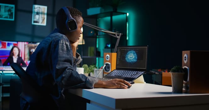 Programmer in living room office typing on keyboard, updating artificial intelligence neural networks, writing binary code scripts. Freelancing system administrator upgrading high tech AI, camera B