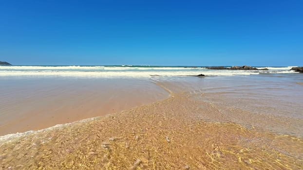 A peaceful and tranquil beach scene capturing the soft, gentle waves along with a vibrant blue sky above