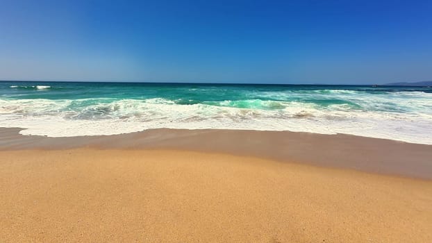 A serene and tranquil beach scene featuring gentle waves lapping against soft golden sand under a clear blue sky