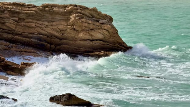 A beautiful shoreline featuring stunning turquoise waters with waves crashing powerfully against rugged rocks