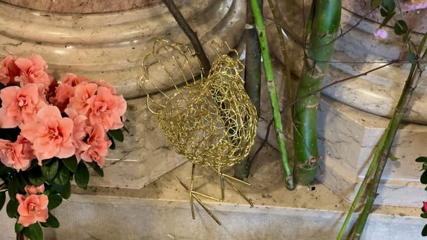 A crafted wire chicken ornament among vibrant flowers, showcasing creativity and charm in its design