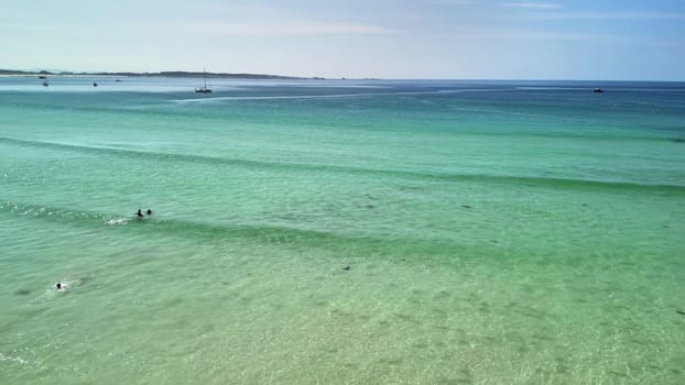 A tranquil beach view highlights the beauty of clear, turquoise waters and people relishing the warm sunlight