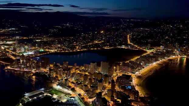 Aerial view of a vibrant coastal city illuminated at night, showcasing beautiful lights and scenery.