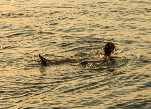 Senior adult man covered with dark mud from the floor of Dead Sea floating in the waters of the salty sea