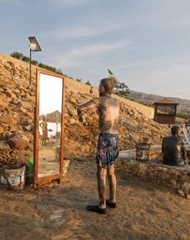Senior adult man spreading dark mud from the floor of Dead Sea which is said to be good for skin care and wrinkles