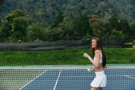 Energetic female athlete in white outfit playing tennis outdoors, exuding joy and health with a beautiful green landscape behind her, ideal for sports and wellness concepts