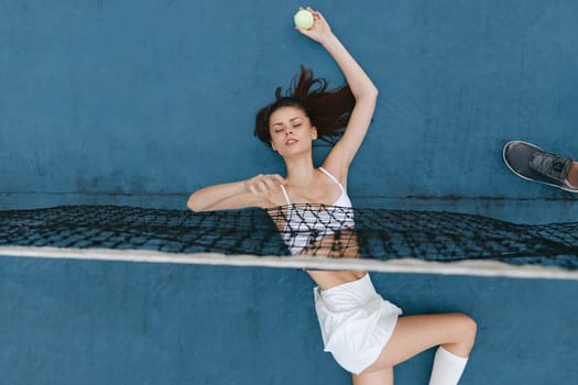 Energetic young woman in a sporty outfit preparing to hit a tennis ball on a vibrant blue court, exuding confidence and focus in her game