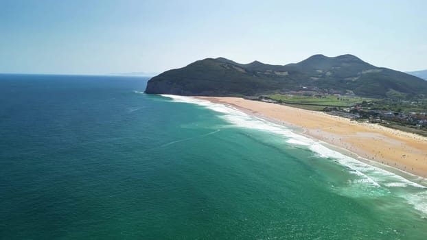 Experience stunning aerial views of a golden beach bordered by majestic mountains and vibrant turquoise waters