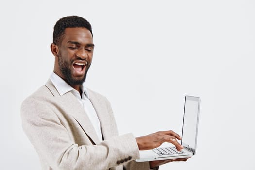 Joyful man with dark skin and curly hair working on a laptop, standing against plain white background, relaxed and confident, casual attire, digital work, modern technology, positivity, lifestyle concept.