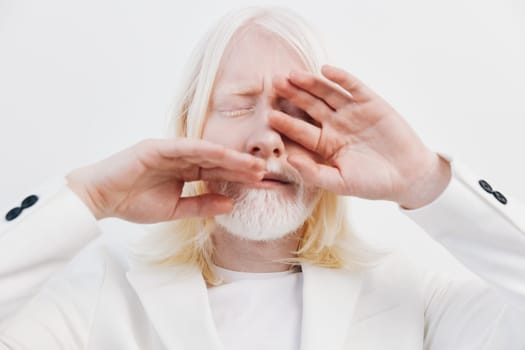 portrait of a serene man with long white hair and a beard, dressed in a white suit, with his eyes closed and hands shielding his face, set against a minimalist white backdrop, evoking calmness