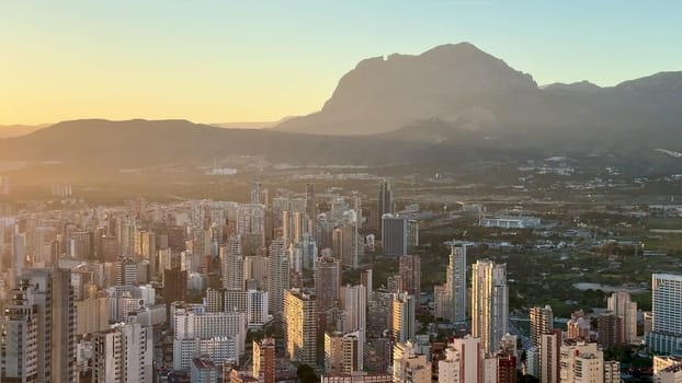 A stunning sunset casts vibrant hues over a bustling city skyline framed by majestic mountains in the background