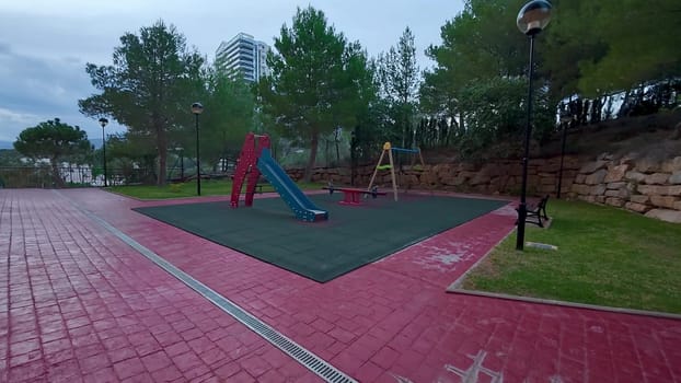 A colorful playground featuring a long slide and several swings is located within a serene park environment