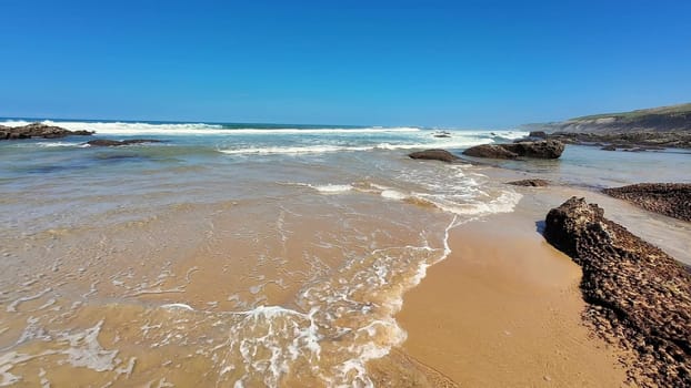 A beautifully serene beach scene featuring clear blue skies, gentle rolling waves, and a warm sandy shore