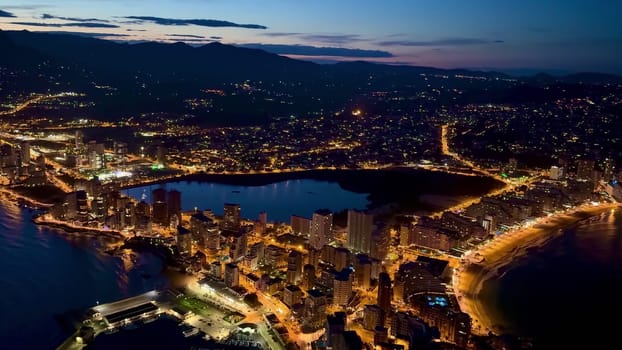 Captivating night aerial shot showcasing a vibrant city with sparkling lights and beautiful coastline.