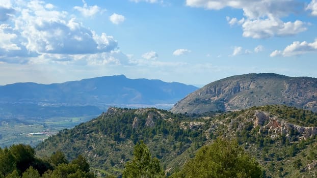 A breathtakingly stunning view of majestic mountains set against a vibrant blue sky filled with fluffy white clouds