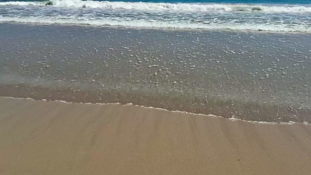 Experience the serene beauty of gentle ocean waves lapping onto a sandy beach beneath vast, clear blue skies