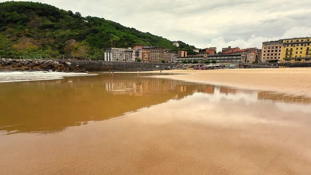 A tranquil beach scene showcasing a picturesque coastal town alongside lush, green hills beneath a cloudy sky