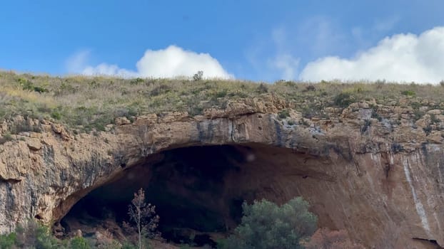 A truly captivating view of a cave entrance beautifully nestled among vibrant lush greenery and rugged rocky terrain