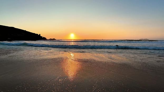 A breathtaking and colorful sunset elegantly casts exquisite golden hues across gentle waves at a tranquil beach