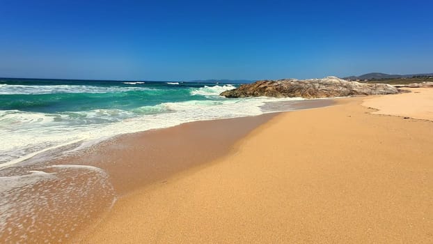 A breathtaking beach landscape showcasing golden sand alongside lively waves beneath a clear, vibrant blue sky