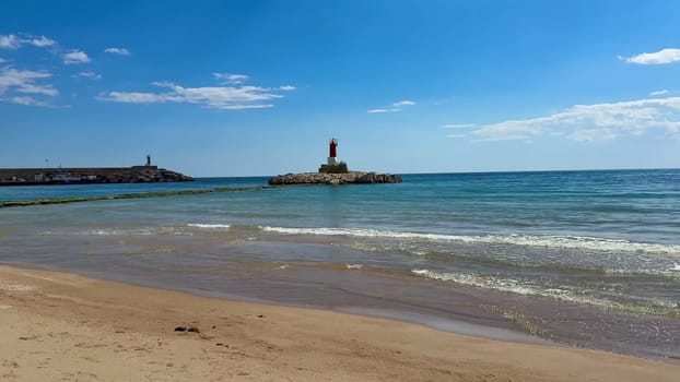 The beautiful coastal scenery showcases a stunning lighthouse, calm tranquil waters, and a vibrant blue sky overhead